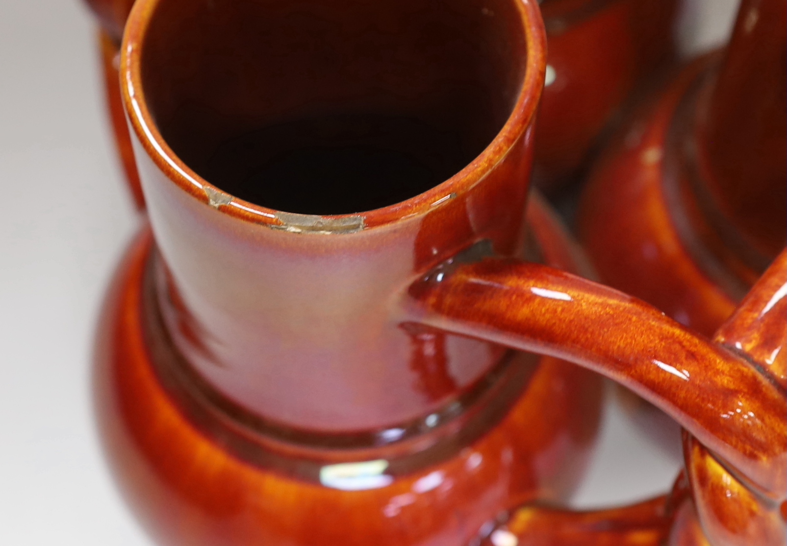 A Burmantofts Pottery three section fuddling cup with interwoven handles in dark burnt orange, stamped with marks to base, height 21cm